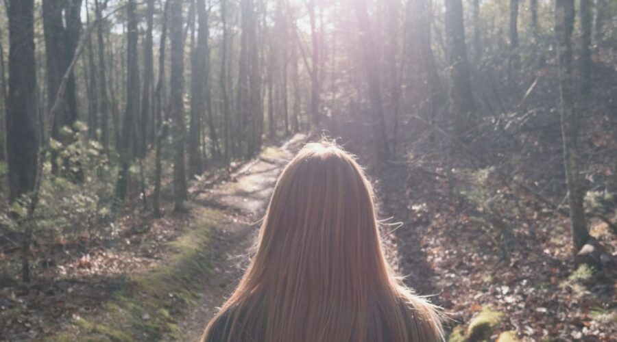 A woman standing in a serene forest, embracing the beauty of nature, symbolizing the importance of environmental wellness. Enhance your environmental wellness with tips on connecting with nature, reducing clutter, and living sustainably.