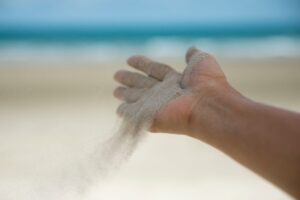 Close-up image of a hand releasing sand, symbolizing the process of letting go of control and embracing trust and uncertainty. This visual metaphor represents the concept of surrendering to the flow of life and accepting what cannot be controlled, as discussed in the blog post on how to embrace uncertainty and reduce anxiety.