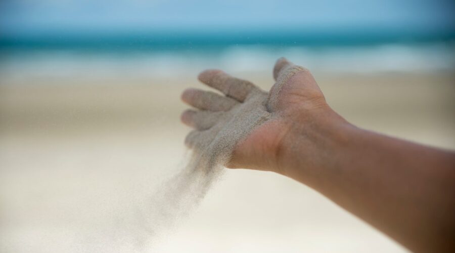 Close-up image of a hand releasing sand, symbolizing the process of letting go of control and embracing trust and uncertainty. This visual metaphor represents the concept of surrendering to the flow of life and accepting what cannot be controlled, as discussed in the blog post on how to embrace uncertainty and reduce anxiety.