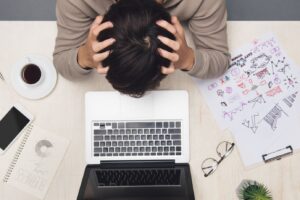 Image of a man with his head in his hands, feeling overwhelmed, representing burnout and work stress therapy in Chicago at Embodied Wellness Center.