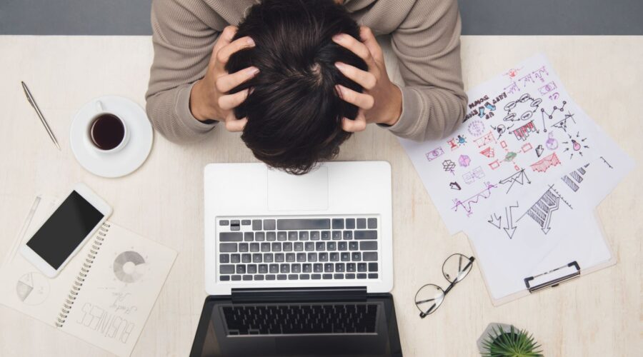 Image of a man with his head in his hands, feeling overwhelmed, representing burnout and work stress therapy in Chicago at Embodied Wellness Center.