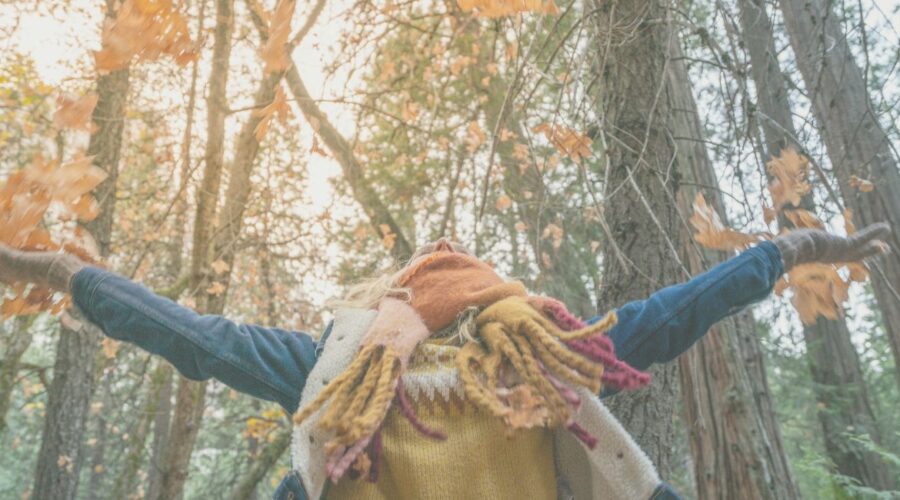 A woman joyfully tosses autumn leaves into the air, symbolizing the practice of letting go during the fall season. This serene image captures the essence of mindfulness and release, aligning with holistic wellness practices such as mindfulness, breathwork, and self-compassion. Ideal for illustrating tips on emotional healing and self-care during the transition of seasons in a "Five Holistic Ways to Practice Letting Go This Fall" blog post.