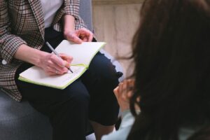 A therapist taking notes while sitting across from a client during a therapy session, highlighting personalized care and a goal-oriented approach to enhancing the therapy experience at Embodied Wellness Center.