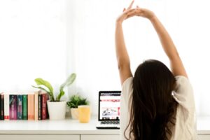 A woman seated at her desk stretches her arms overhead, practicing desk yoga to relieve stress and improve posture. This image illustrates a simple office-friendly yoga pose, perfect for reducing tension, enhancing circulation, and boosting focus during the workday. Featured in the "Desk Yoga: 6 Simple Poses to Relieve Stress and Boost Productivity" blog post from Embodied Wellness Center, where practical tips for incorporating mindfulness and holistic wellness into your daily routine are shared.