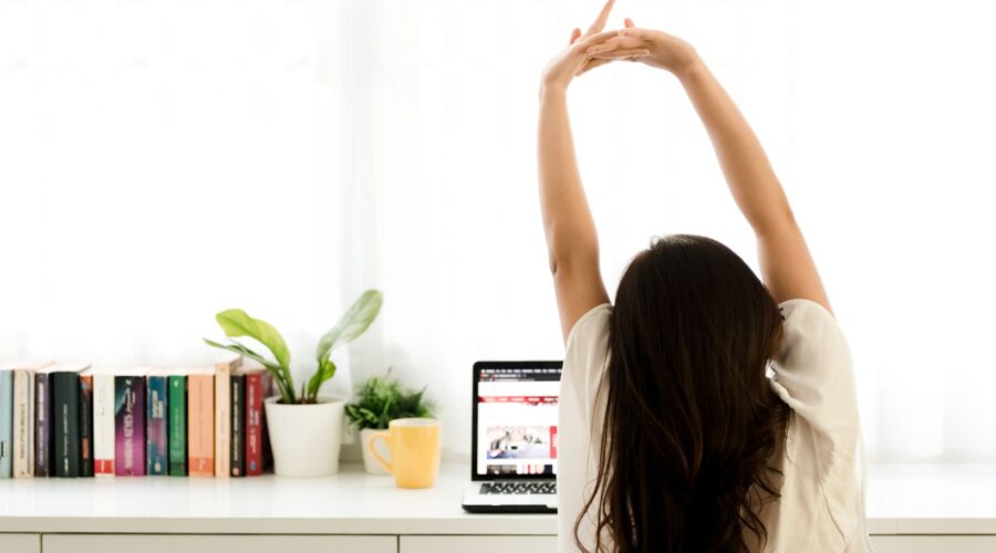 A woman seated at her desk stretches her arms overhead, practicing desk yoga to relieve stress and improve posture. This image illustrates a simple office-friendly yoga pose, perfect for reducing tension, enhancing circulation, and boosting focus during the workday. Featured in the "Desk Yoga: 6 Simple Poses to Relieve Stress and Boost Productivity" blog post from Embodied Wellness Center, where practical tips for incorporating mindfulness and holistic wellness into your daily routine are shared.