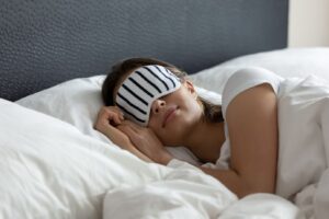 A peaceful woman sleeping in bed with soft lighting, wrapped in a cozy blanket, symbolizing relaxation and a quiet mind after practicing mindfulness techniques for better sleep.