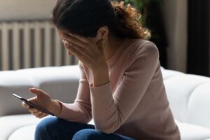 Upset woman looking at her phone, feeling anxious from doomscrolling negative news—illustrating the emotional toll of excessive media consumption.