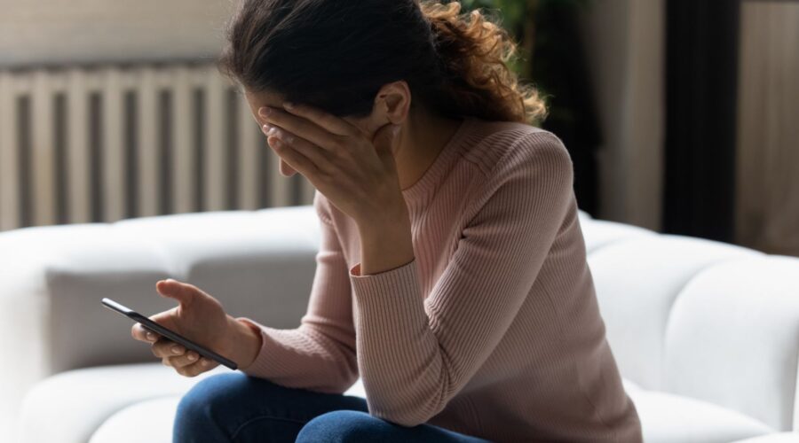 Upset woman looking at her phone, feeling anxious from doomscrolling negative news—illustrating the emotional toll of excessive media consumption.