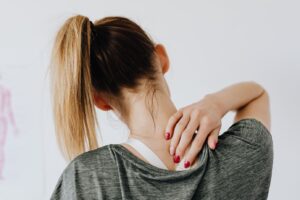 A woman gently holding the back of her neck in discomfort, illustrating common neck and shoulder tension caused by stress or poor posture—featured in our blog on simple stretches to relieve upper body tension.