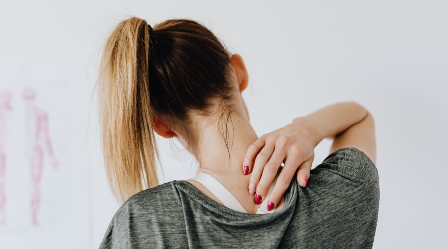 A woman gently holding the back of her neck in discomfort, illustrating common neck and shoulder tension caused by stress or poor posture—featured in our blog on simple stretches to relieve upper body tension.