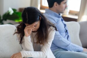 A couple sitting on the couch facing away from each other after an argument, showing conflict in a relationship.