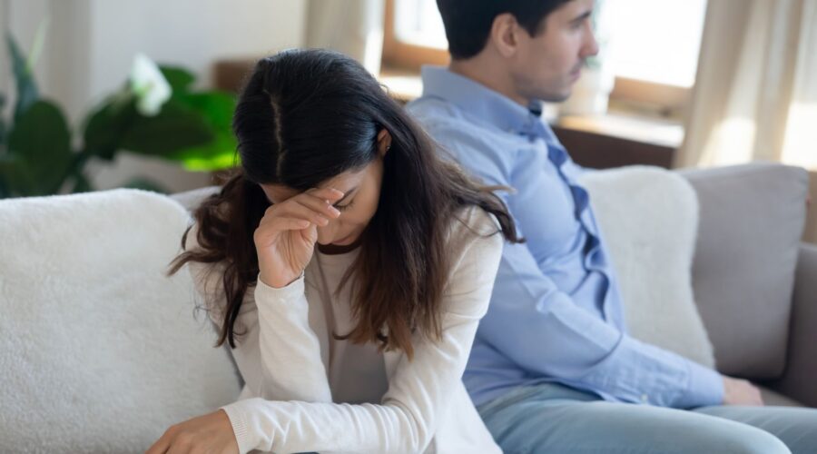 A couple sitting on the couch facing away from each other after an argument, showing conflict in a relationship.