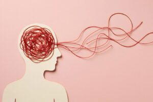 Abstract illustration of a human silhouette with tangled red lines inside the head flowing outward, symbolizing racing thoughts, anxiety, and mental overwhelm—representing cognitive defusion exercises that help create distance from intrusive thoughts and get unstuck in your head.