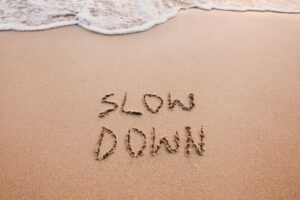 The words ‘Slow Down’ written in sand as ocean waves approach, symbolizing mindfulness, relaxation, and taking life at a calmer pace.