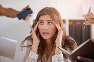 Woman looking overwhelmed while multiple people ask for her attention, representing the stress and anxiety that can come from people-pleasing and trying to meet everyone’s expectations.
