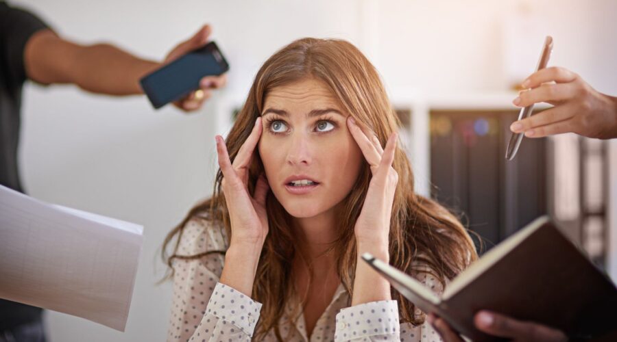 Woman looking overwhelmed while multiple people ask for her attention, representing the stress and anxiety that can come from people-pleasing and trying to meet everyone’s expectations.