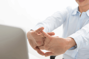 Person stretching hands and wrists at a desk to release body tension between meetings and reduce stress while working on a laptop.