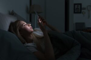 A woman scrolling on her phone, representing doomscrolling, social media overload, and the impact of consuming stressful online content on mental health and the nervous system.