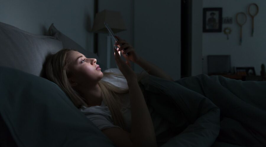 A woman scrolling on her phone, representing doomscrolling, social media overload, and the impact of consuming stressful online content on mental health and the nervous system.