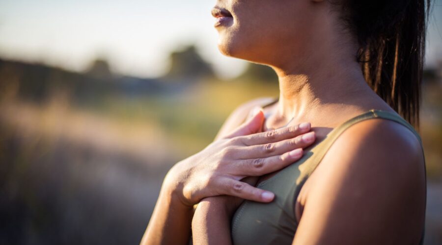 Woman practicing self-compassion with her hands over her heart while taking a calming breath outdoors